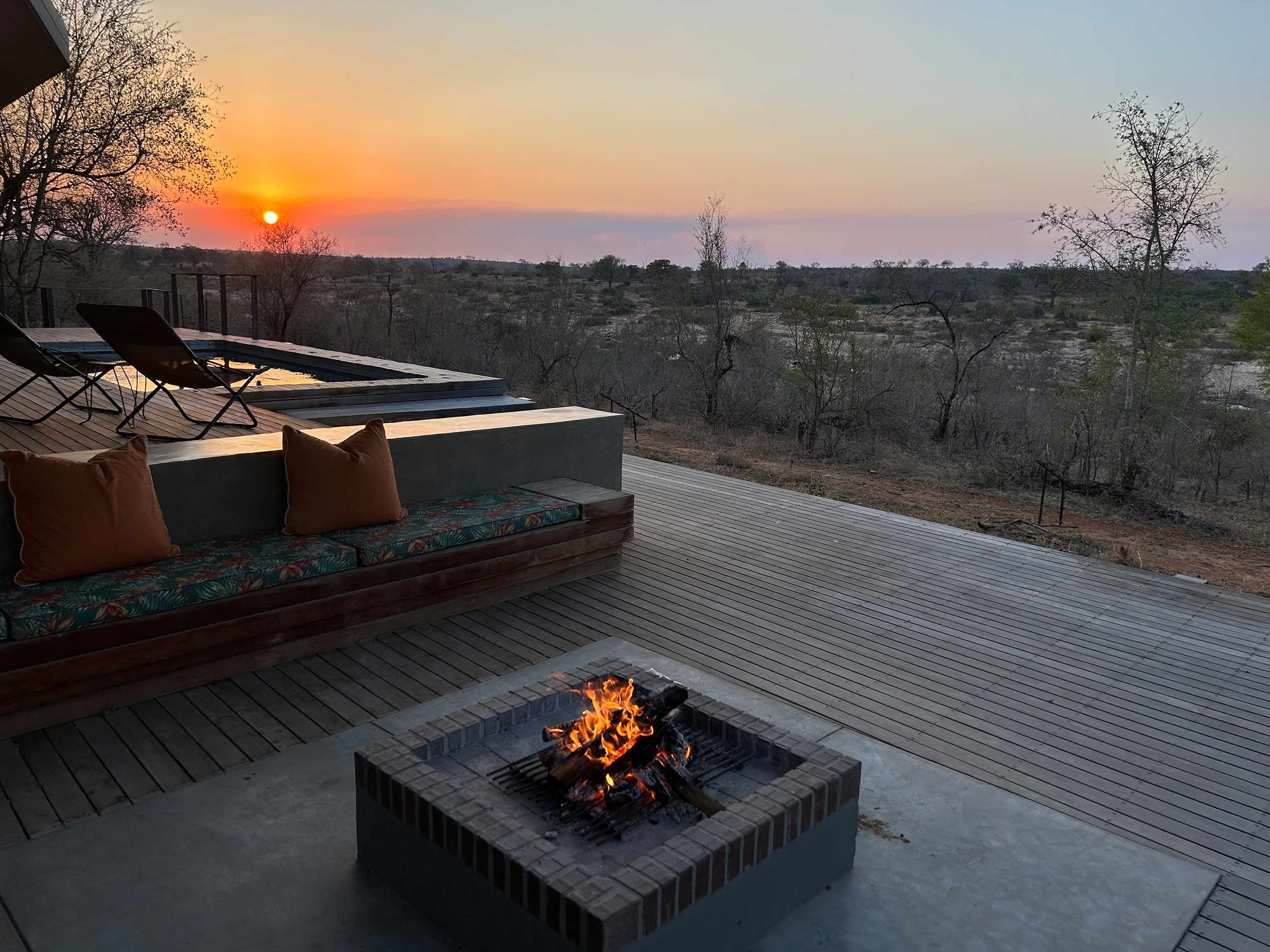 Outdoor deck with a fire pit, seating area, and two lounge chairs near a small pool, overlooking a scenic view at sunset.