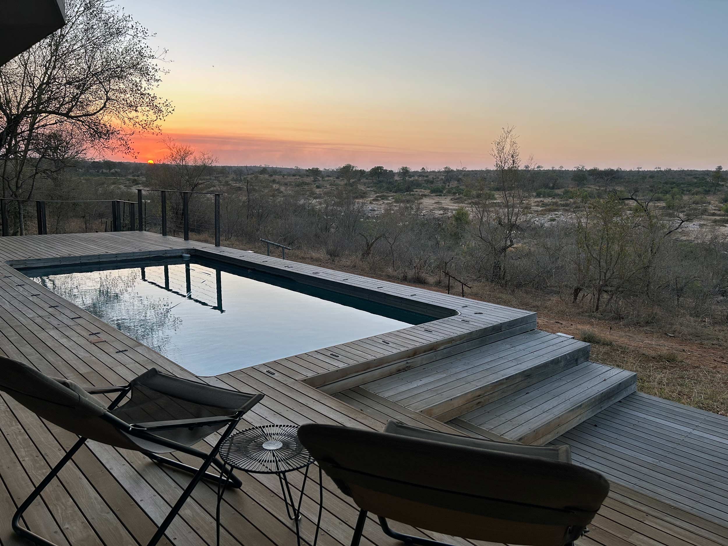 Deck with swimming pool overlooking a scenic landscape at sunset, with trees and open fields in the background.